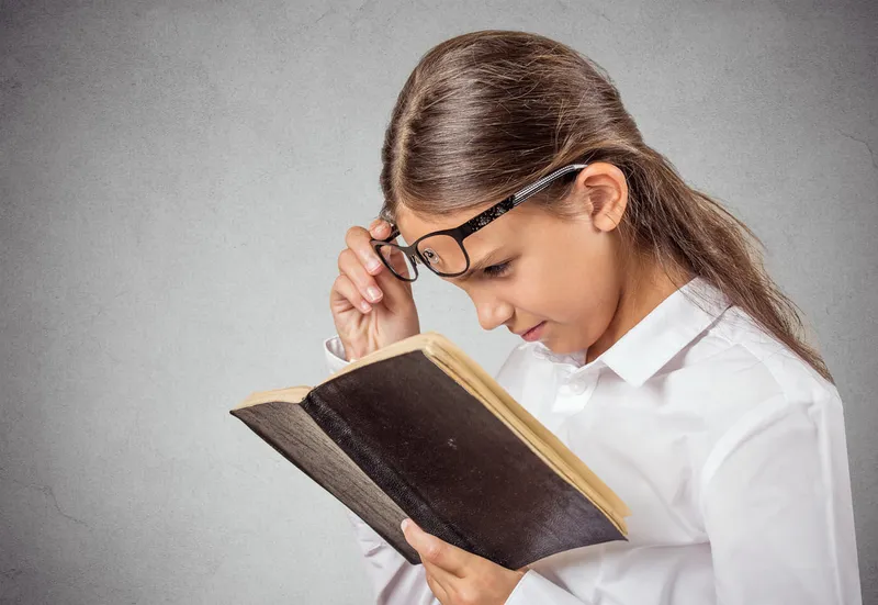 dziewczynka czytająca książkę w okularach